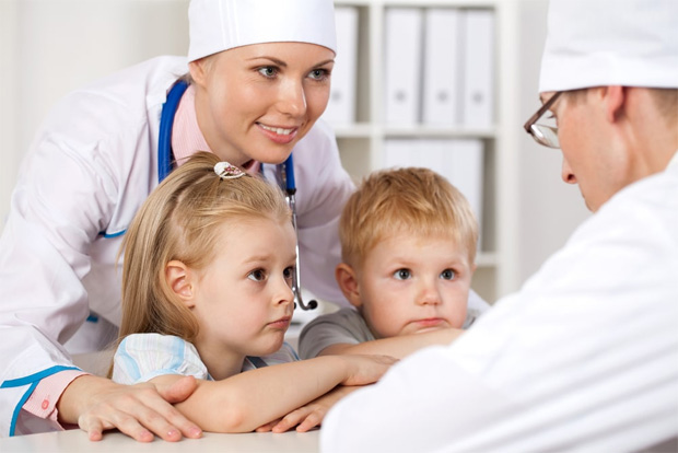 Медсестра обнимает двух детей, которые беседуют с доктором